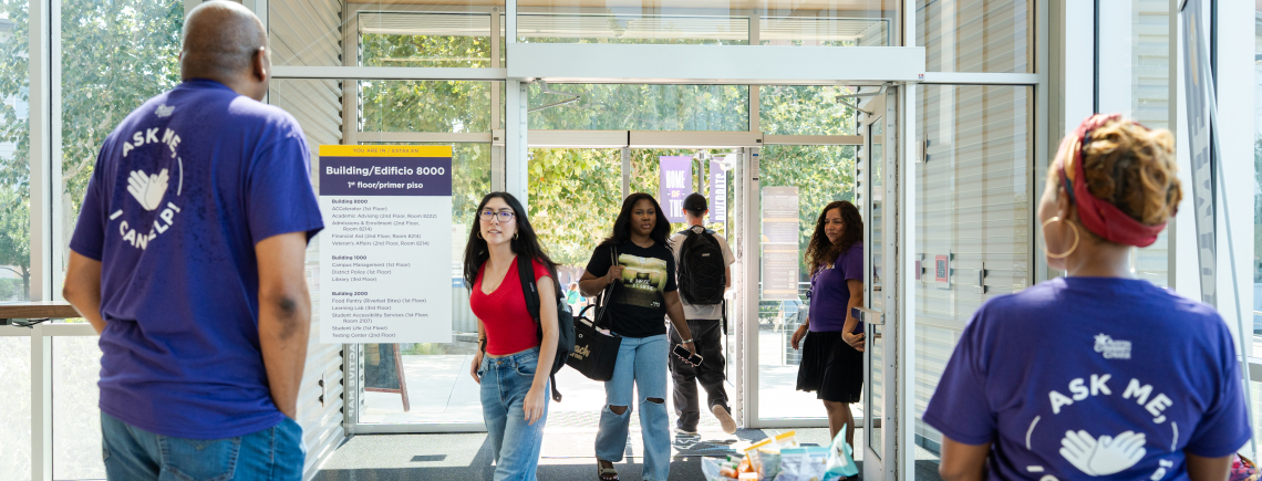 Several students come on to campus and are greeted by staff with teachers that say Ask Me, I Can Help