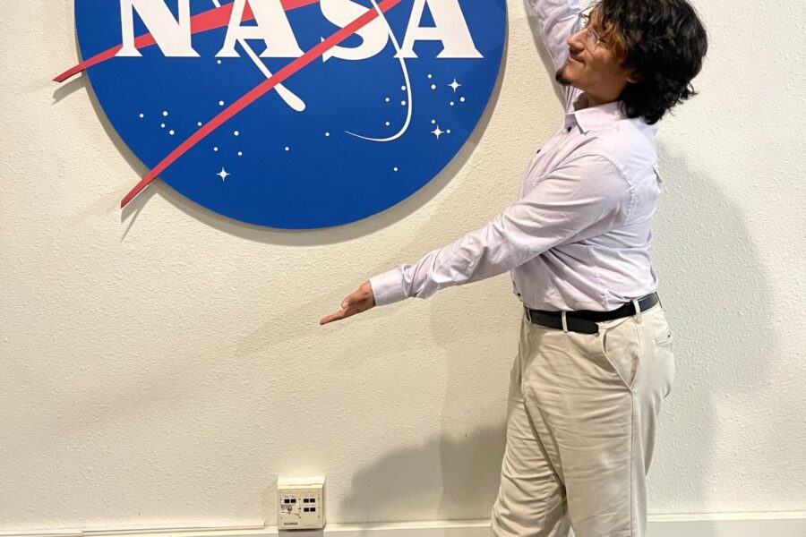 Student participating in NASA Community College Aerospace Scholars (NCAS) program pose for picture in front of NASA sign