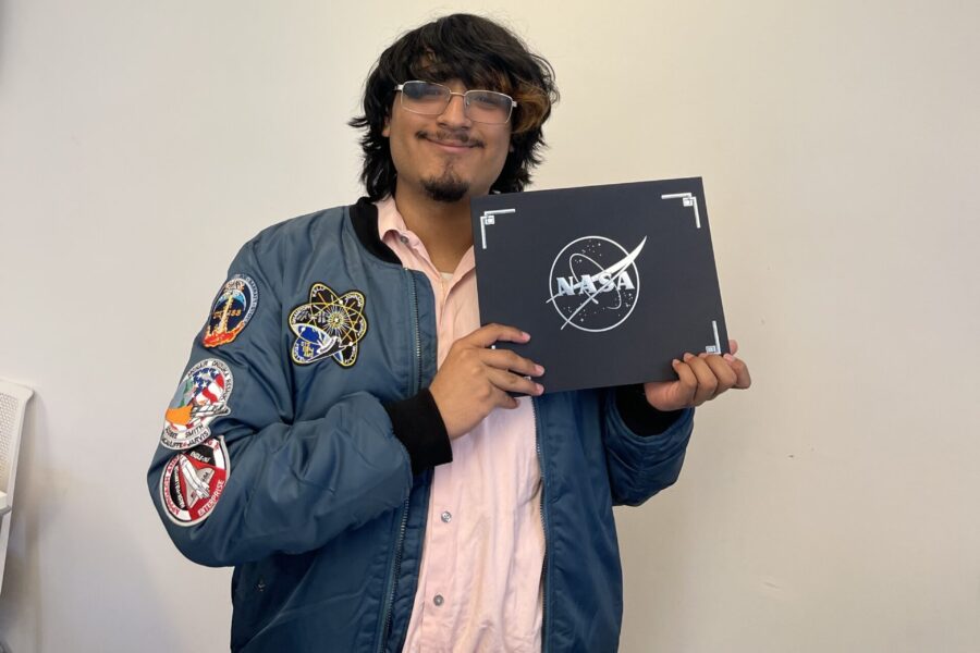 Student participating in NASA Community College Aerospace Scholars (NCAS) program pose for picture in front of NASA sign
