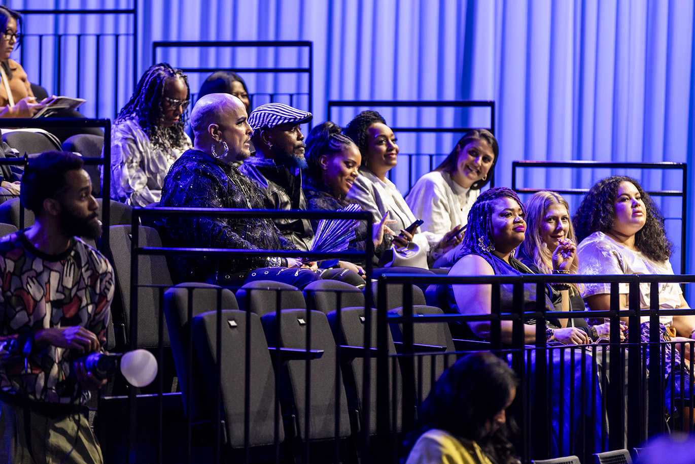 Fashion Show Image of a dozen people in the crowd preparing for models to start walking the runway.