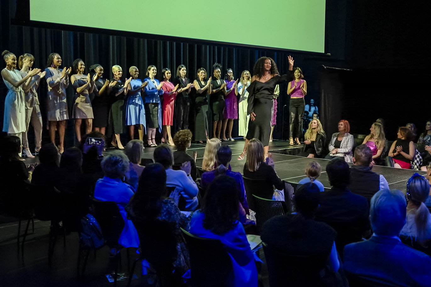 Fashion Show ACC Fashion Incubator Director Nina Means waves to the crowd in front of group of women at fashion show.