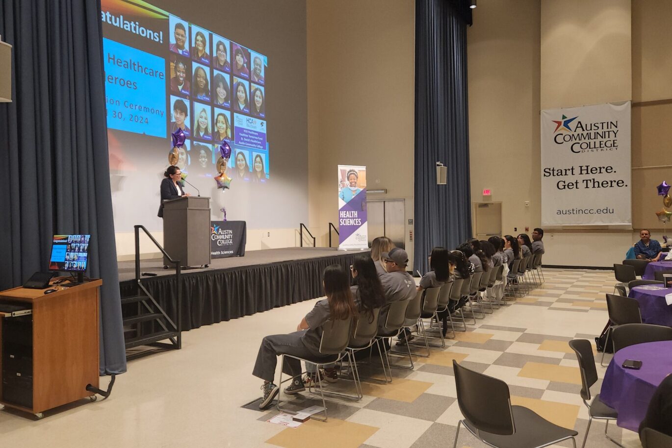 nina and group seated Future Healthcare Heroes student graduates look on as speak is on stage