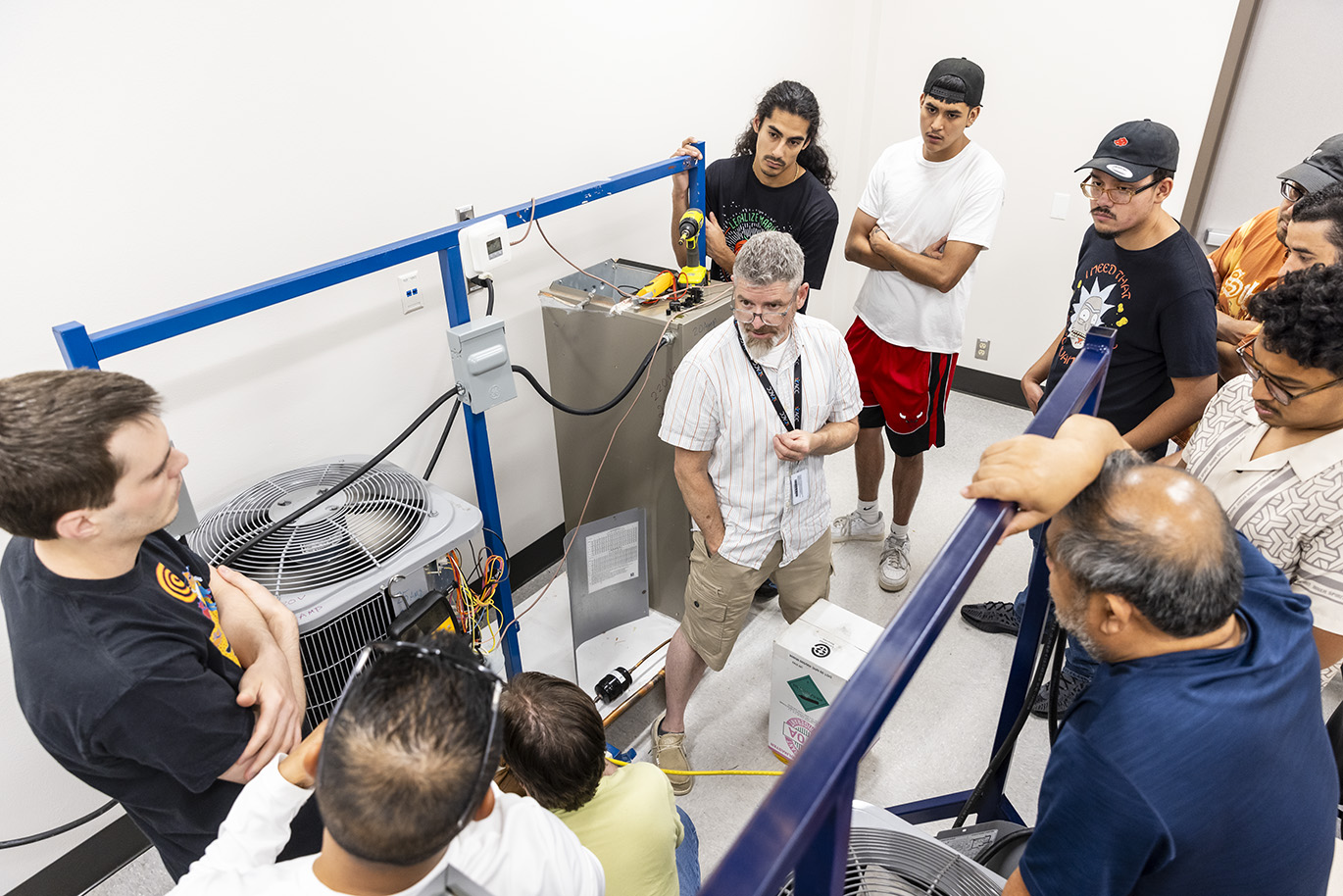 College instructor teaches a lab while standing in the middle of a group of students who from a circle around him.