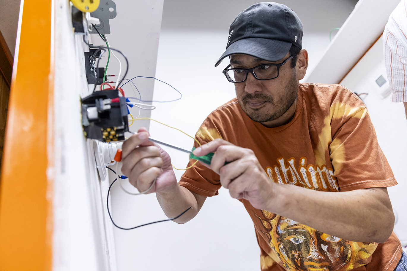 An adult age male college student uses a screwdriver while working on an electrical circuit.