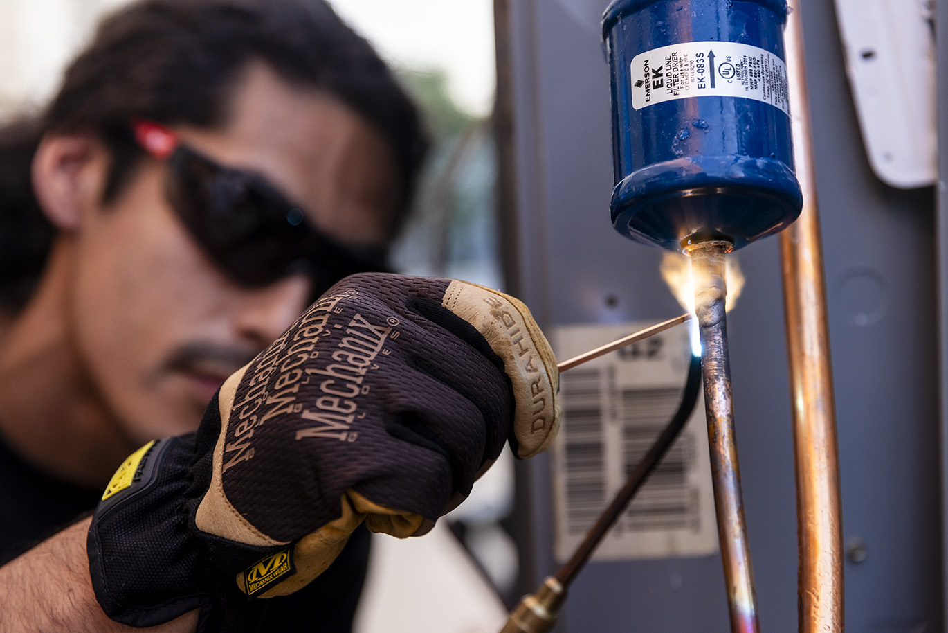 Up close detail image of an adult age male student wearing protection glasses and gloves practices brazing, a process used in the Heating, Ventilation, and Air Conditioning industry to join two or more pieces of metal together by heating them with a blow torch.