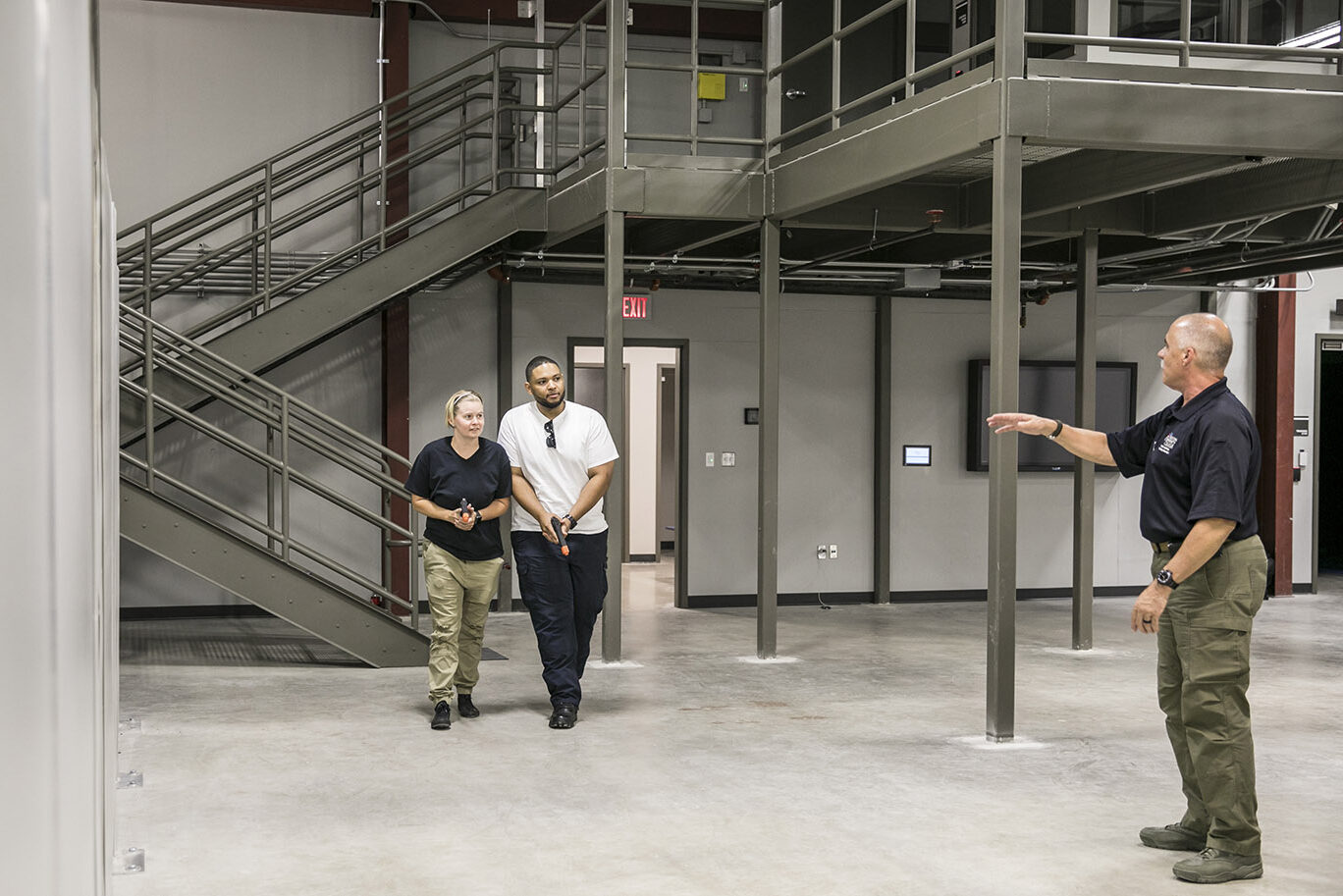 An instructor gives directions to two adult students who hold plastic non-live fire hand guns during a force on force tactical training.