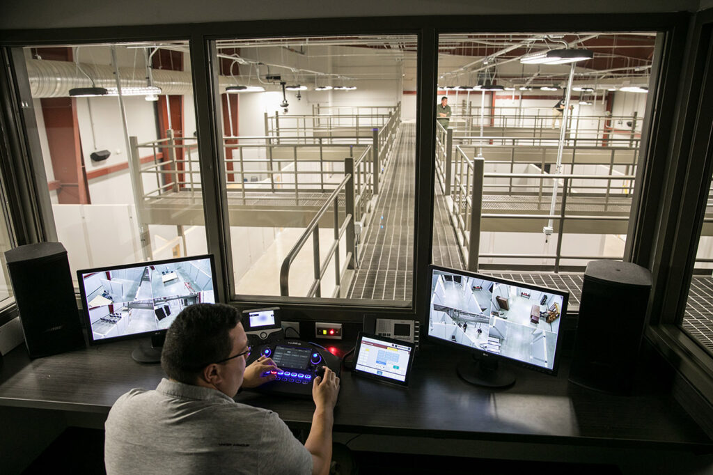 A man monitors two screen inside a tactical training facility contour room.