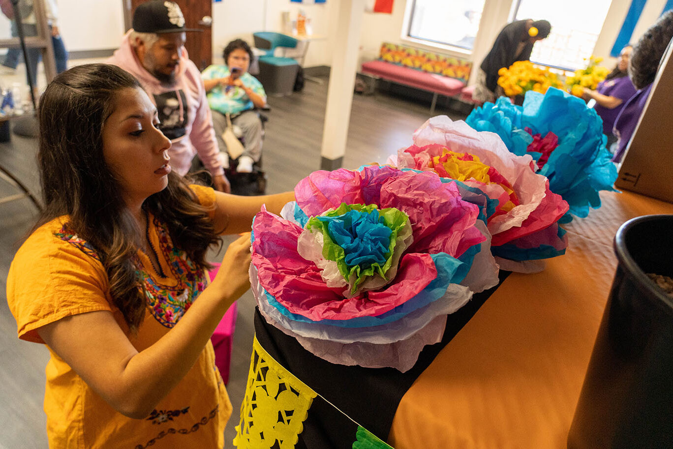 A woman wearing a traditional Mexican blouse decorates an altar for Dia de los Muertos.