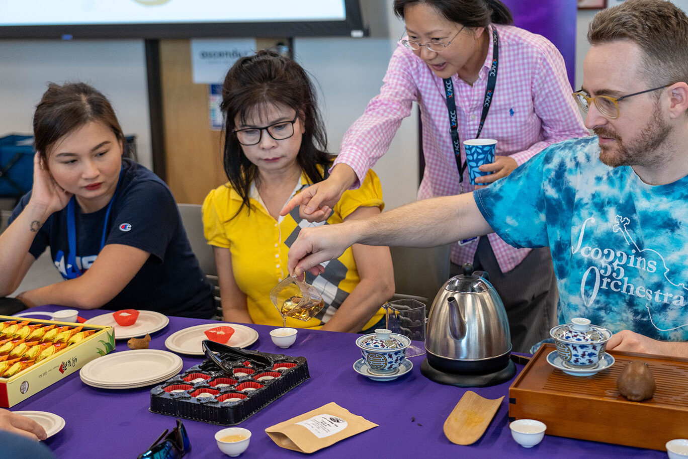 A woman teaches a tea pouring technique attendants of a traditional Chinese tea preparation ceremony event.