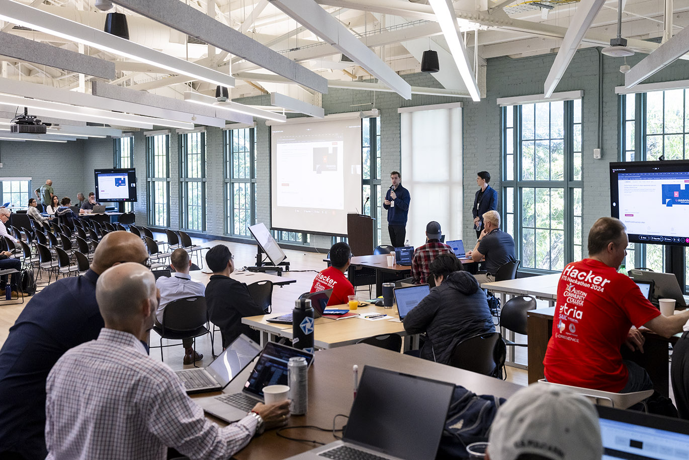 A speaker address attendees inside a large room during a cybersecurity focused hackathon event.