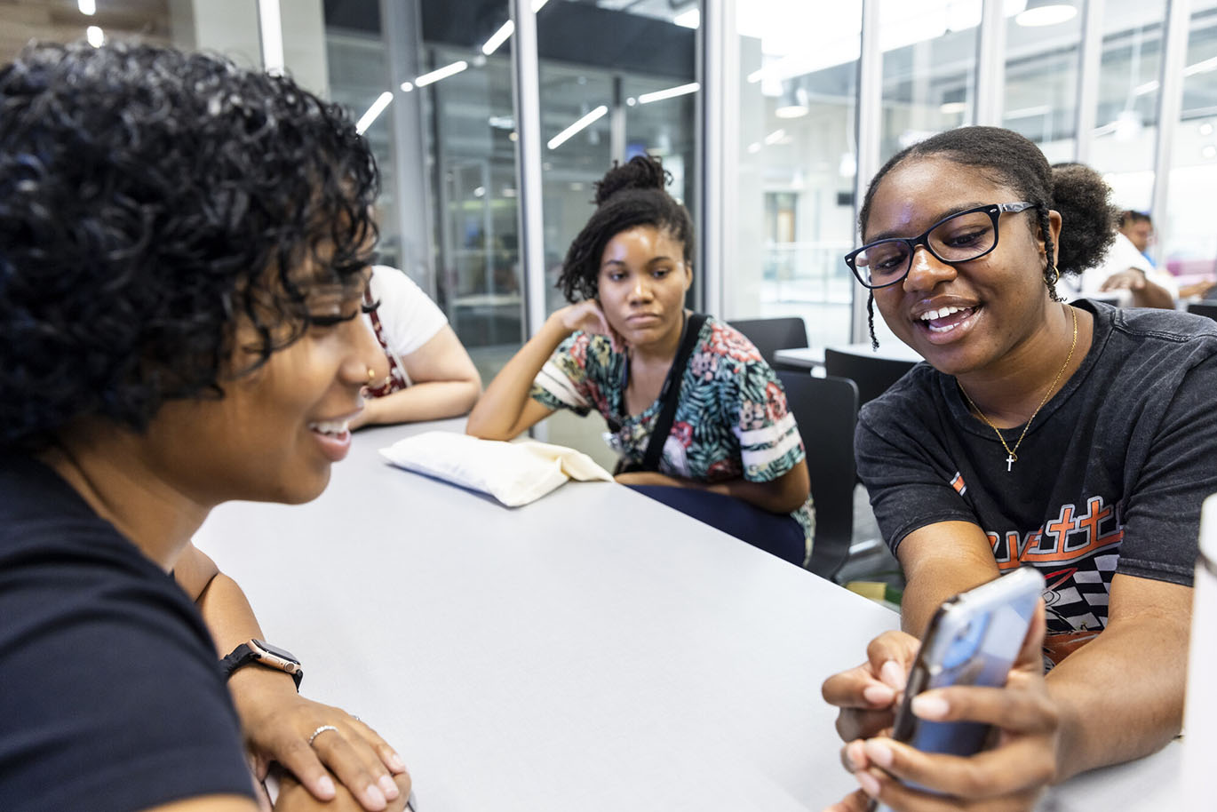 BRASS 2024 Orientation A female college student shows her phone screen to two other college students while seated together at the same table.
