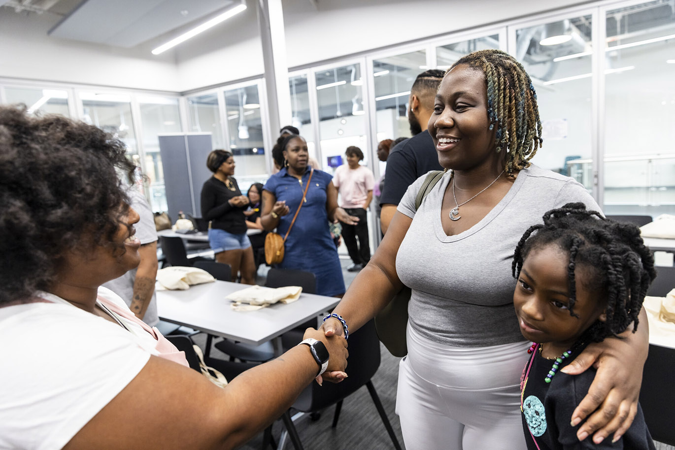 BRASS 2024 Orientation A female college student with her son by her side shakes hands with another female college student during an orientation event.