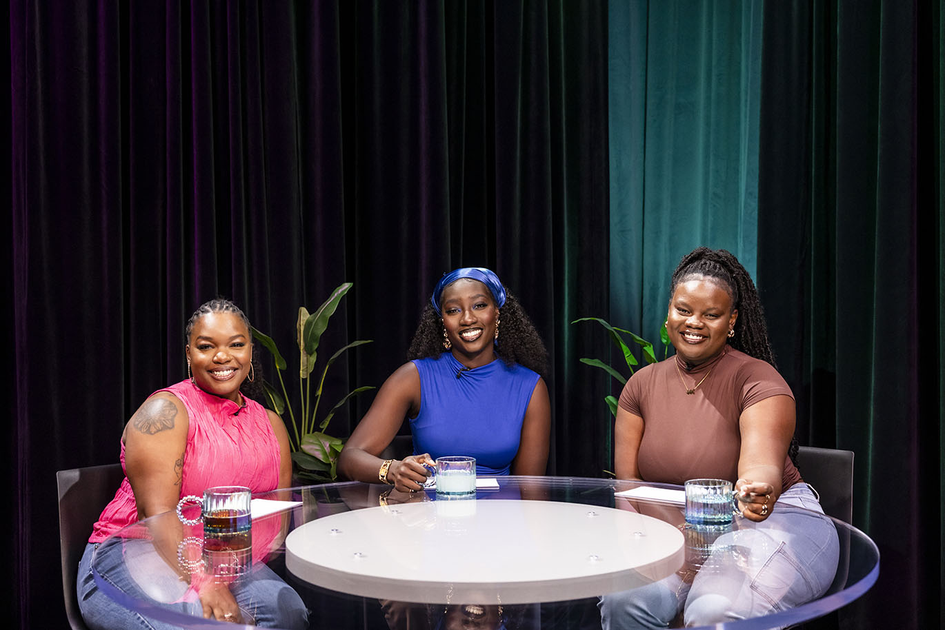 Three female student TV hosts smile and pose together for a group portrait on set.