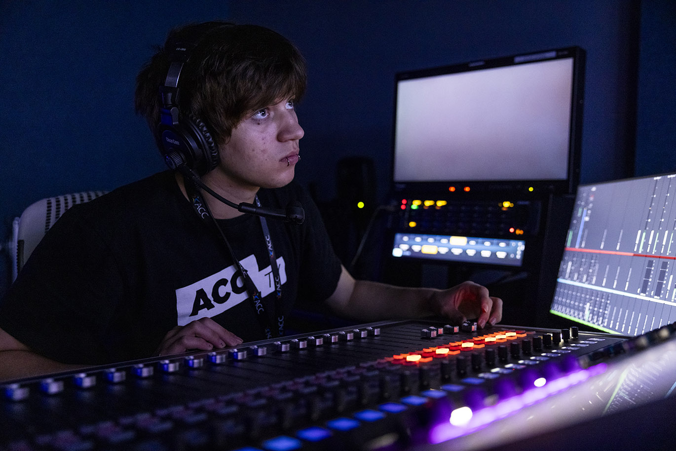 A male TV student intern is seen working with a soundboard inside a control room.