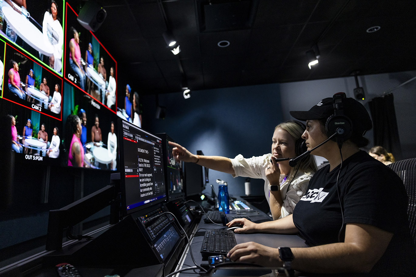 A female TV producer and a female student intern work together inside the control room during the taping of a television show.