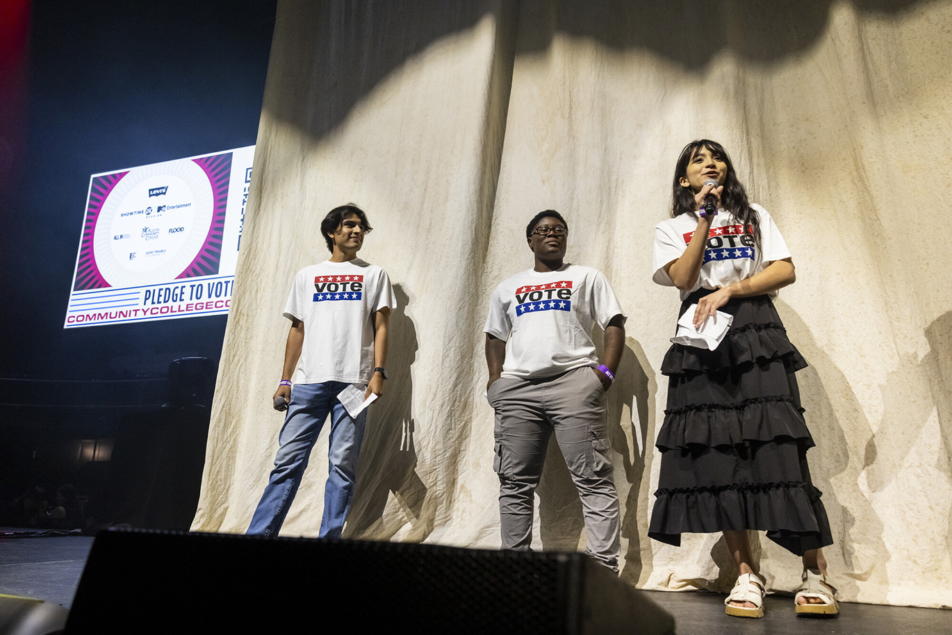 Jessie Murph - Vote Early Concert Three college students wearing white t-shirts with the "Vote" message printed on them as seen on a stage. One of the students is talking into a microphone.