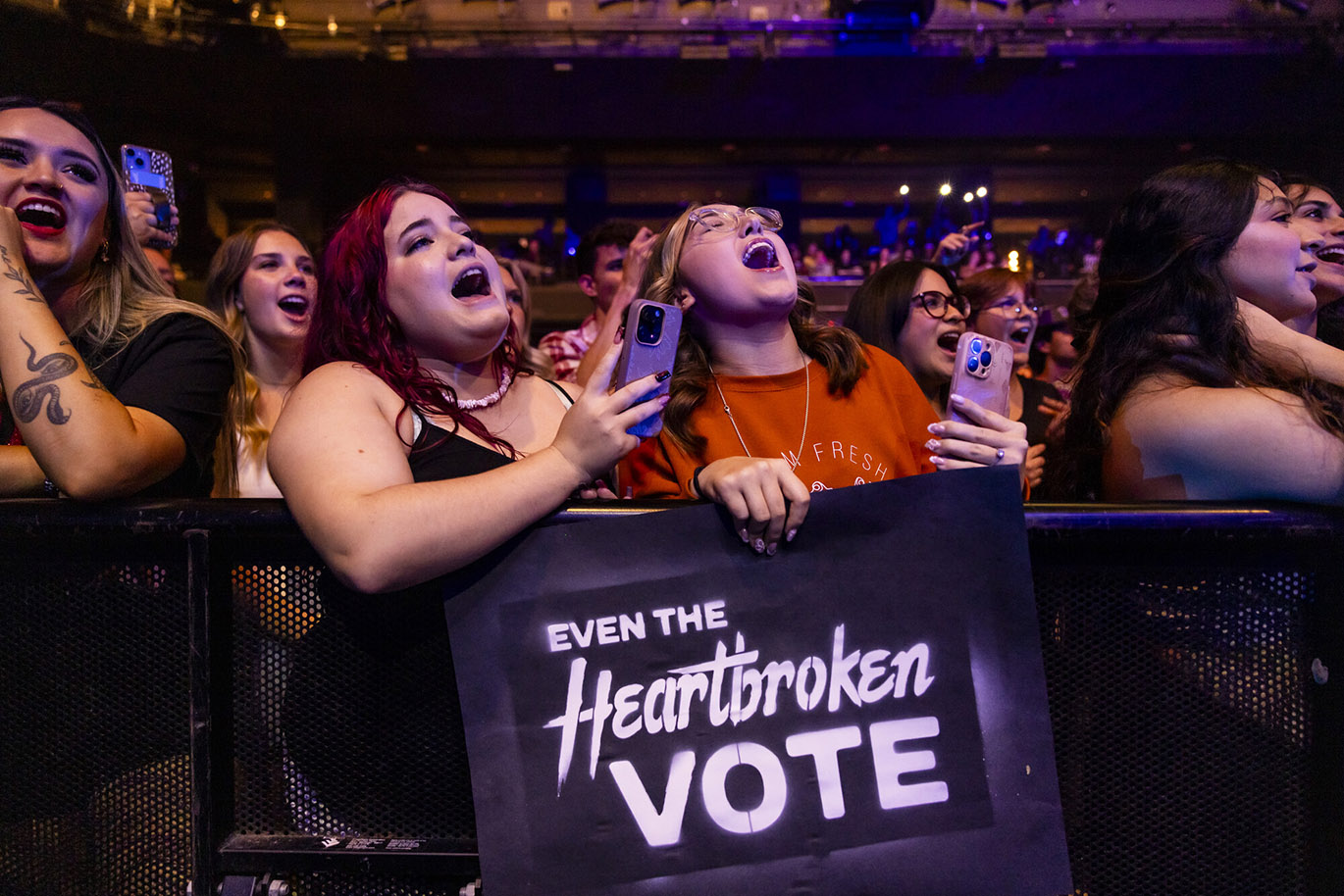 Jessie Murph - Vote Early Concert Two young women sing along during a concert while holding a cardboard sign with the "Even the Heartbroken Vote" message stenciled on it.