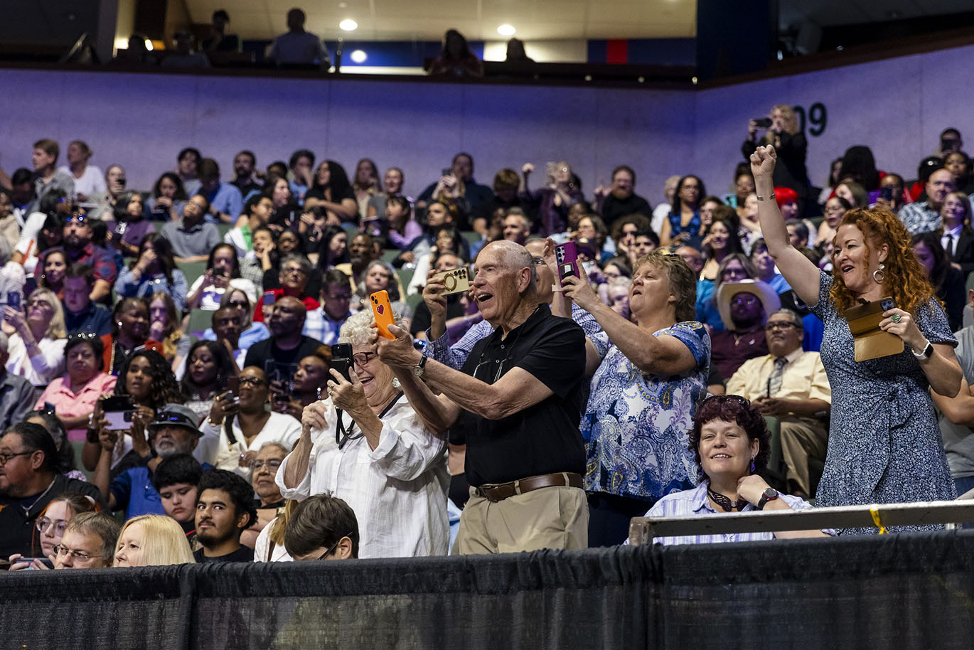 Relatives of a graduate stand up and cheer from the stands during a commencement event.