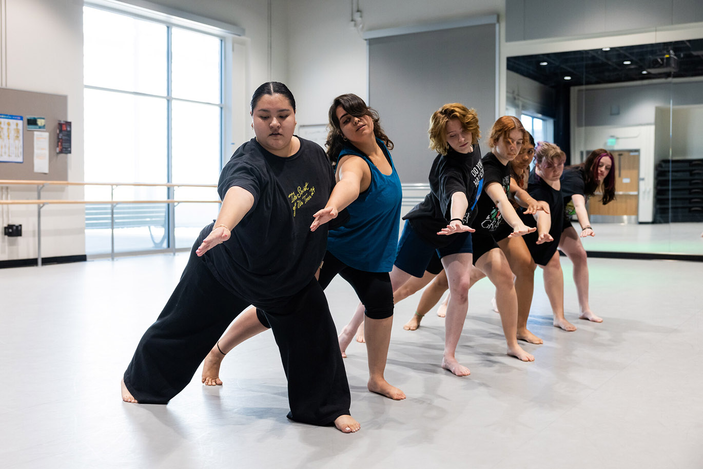 A group of female college students practice dancing in unison during a dance performance class inside a studio.