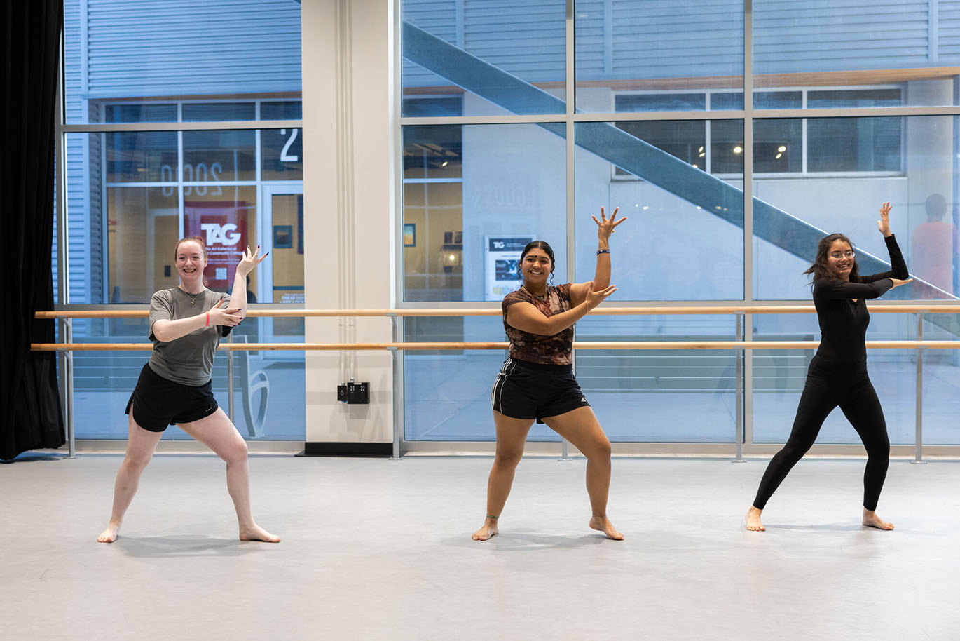 Three female college students look engaged and joyful as they practice dance moves during a beginning jazz class inside a studio.