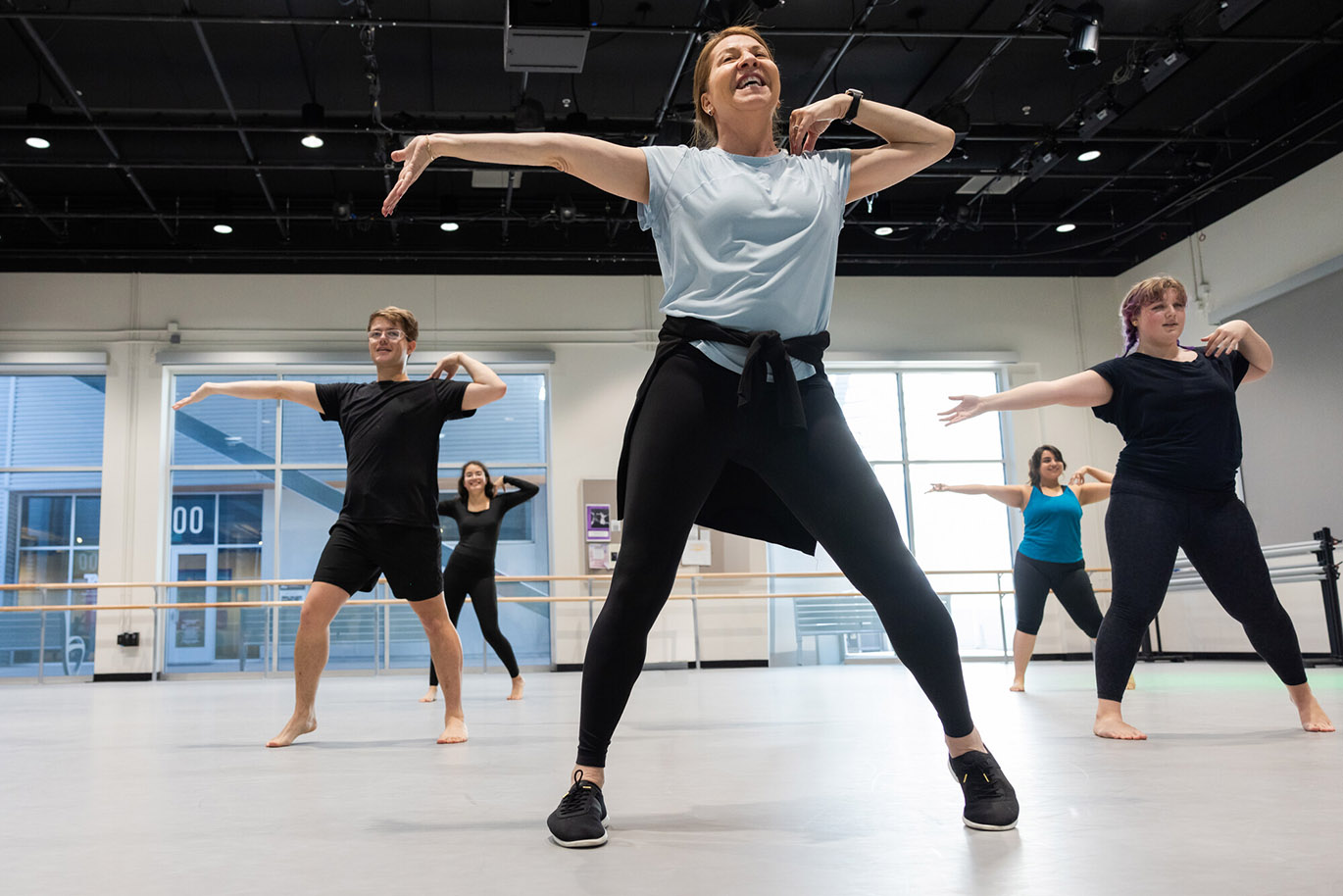 A female college dance instructor female leads a group of students during a beginning jazz class inside a studio.