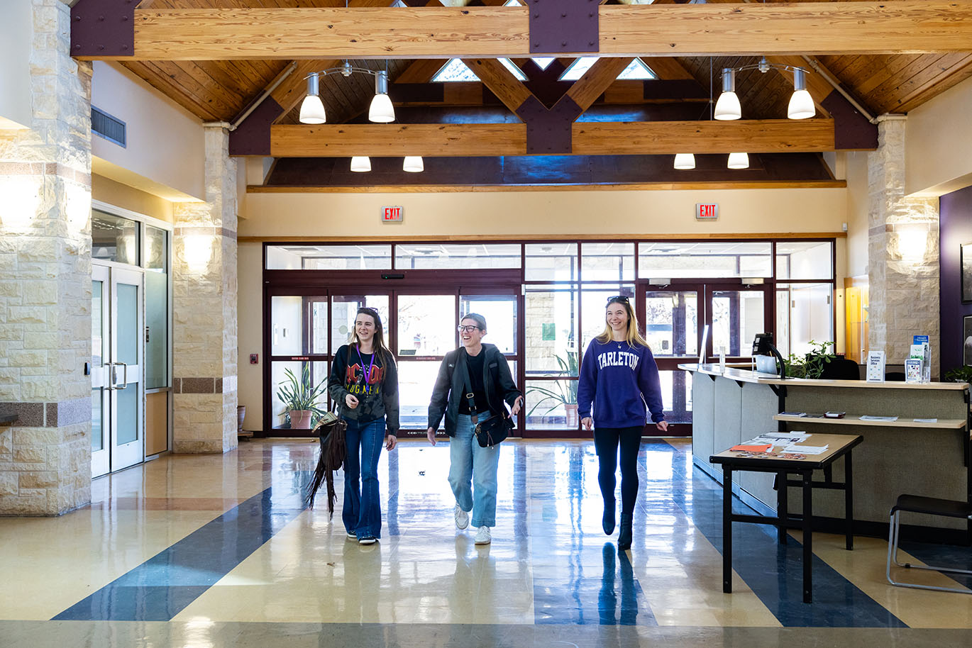Three female ACC students smile and laugh as they walk together into the main area of a campus building, appearing cheerful and engaged.