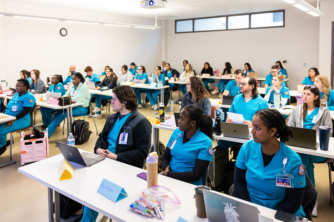 A classroom filled with male and female ACC students, all wearing scrubs, seated at their desks.