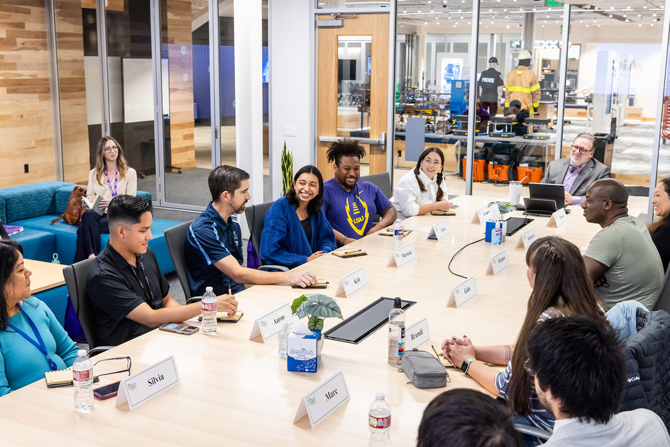 A diverse group of college students, representing various ages, genders, ethnicities, and races, is seated at a conference table, engaged in conversation. Most of the students are smiling. At the end of the table sits ACC Chancellor Dr. Russell Lowery-Hart.