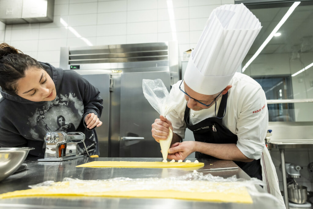 ACC student poses with Chef while making pasta in kitchen