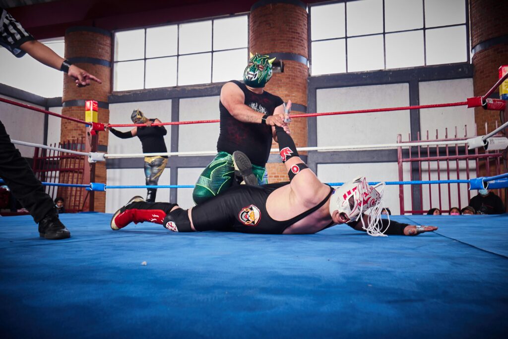 A luchador pins down another luchador while the referee does the countdown