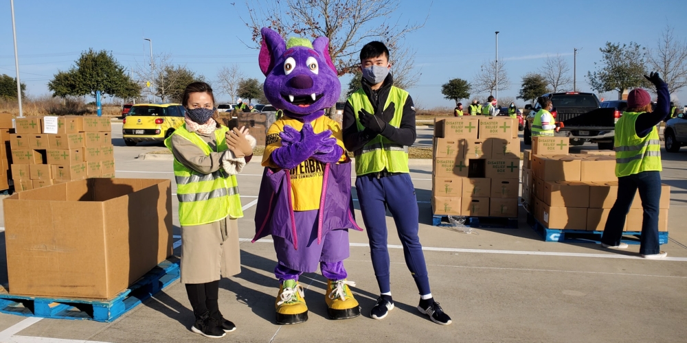 RB standing in the center between two volunteers holding up their bat hands at a food distribution