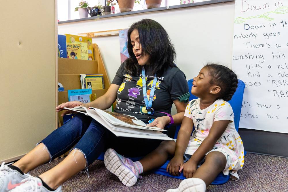 A woman and a child sit on the floor, engrossed in reading books together, surrounded by a cozy atmosphere.