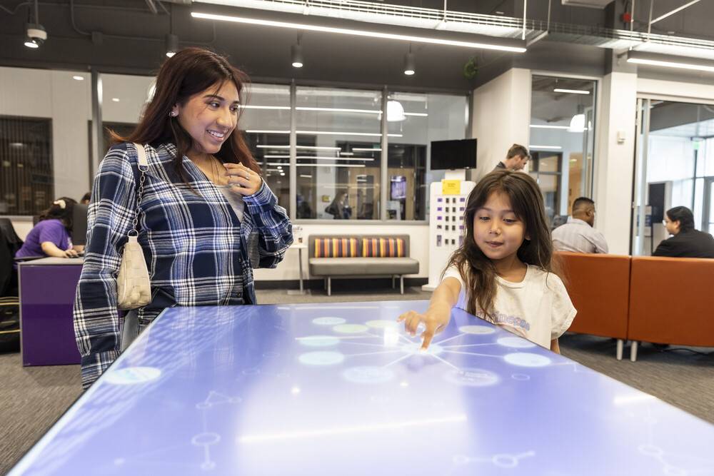 A woman and a child engage joyfully with an interactive table, exploring its features together in a playful environment.